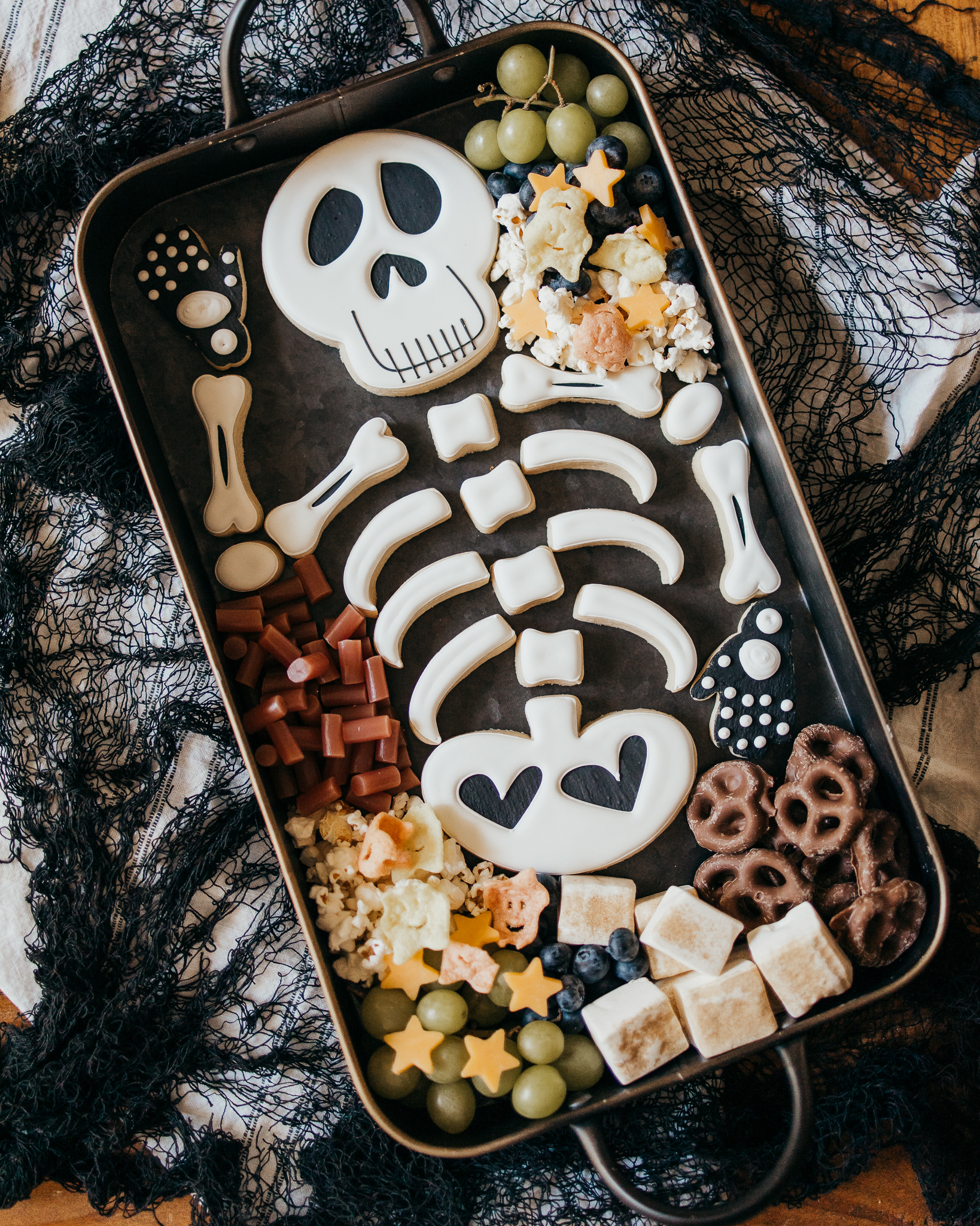 charcuterie board featuring a skeleton cookie, various fruit, sweet treats, and cheese