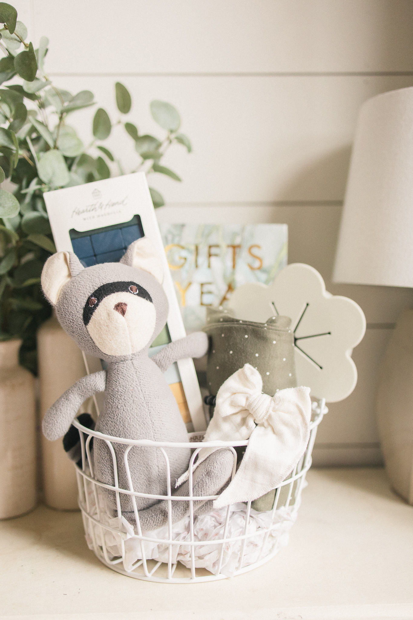 white wire basket with hair bow, olive dot pajamas, stuffed animal, book, and wooden stacking game inside
