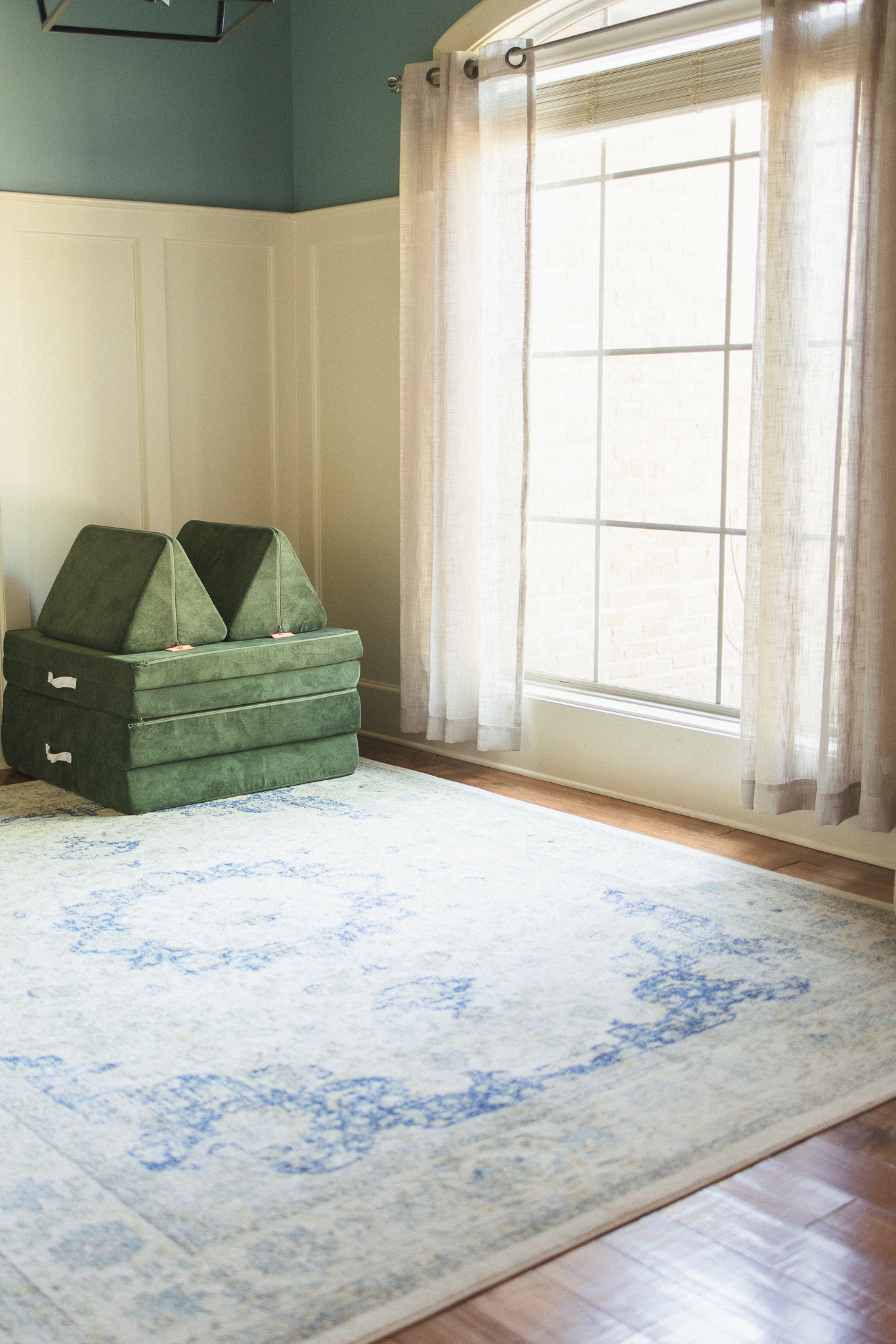 image of empty room with a moss green play couch stacked in the corner and natural light filling the room