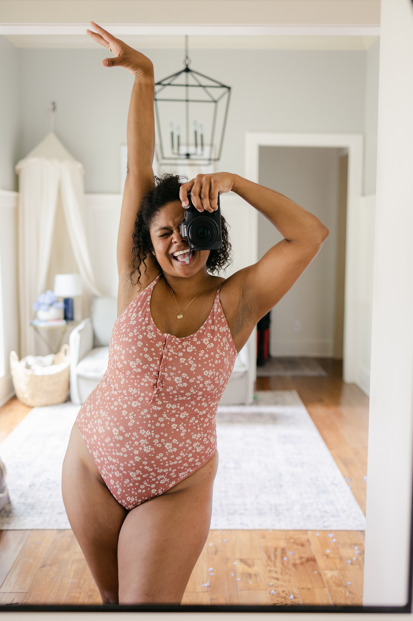 Black woman looking excited taking a self portrait in a mirror of pink and white floral one piece swimsuit