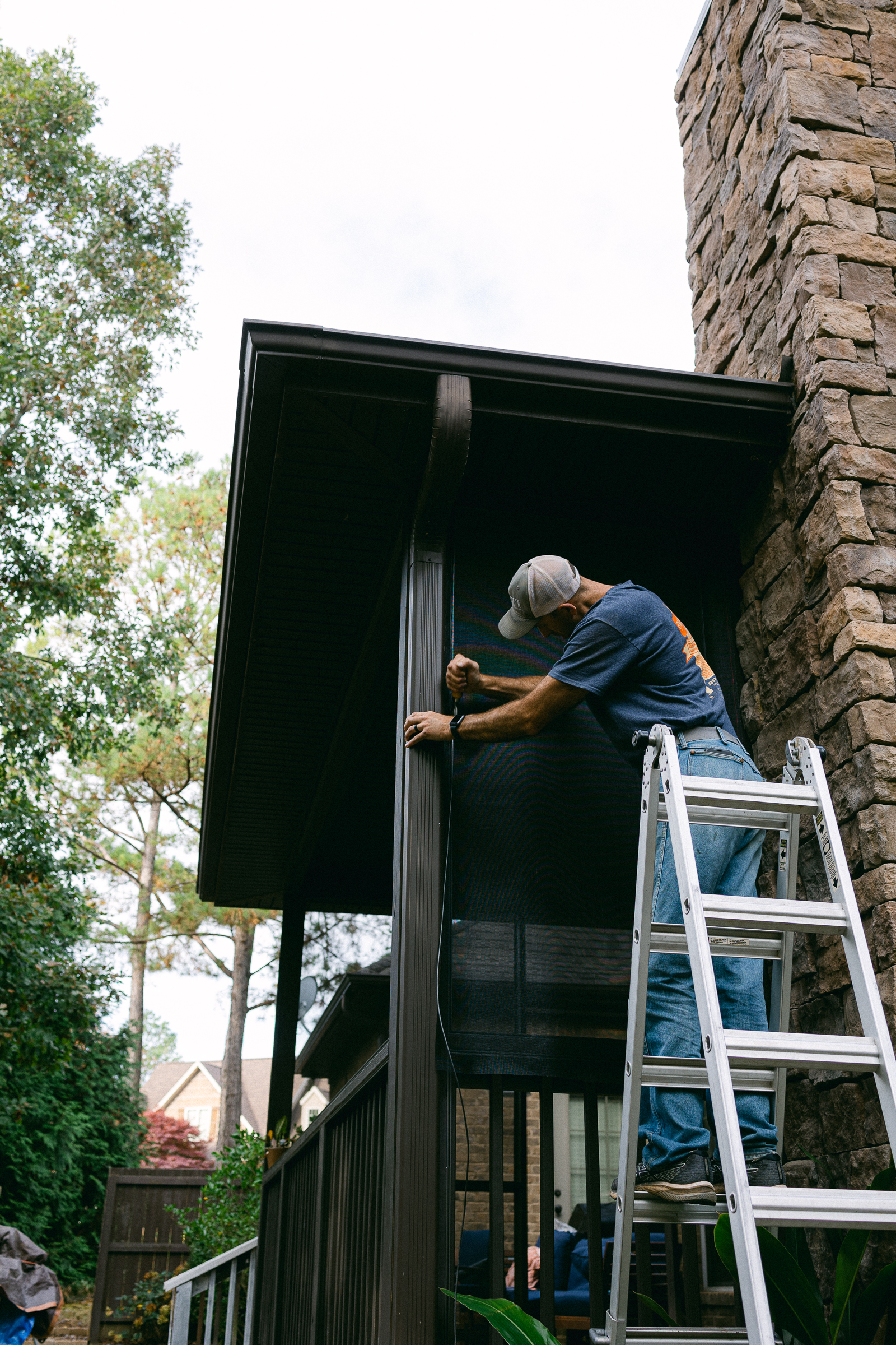 man on tall ladder installing screened porch